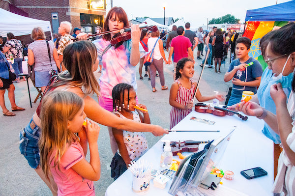 A violinist plays on the street in Benson while children do a craft activity at a table.